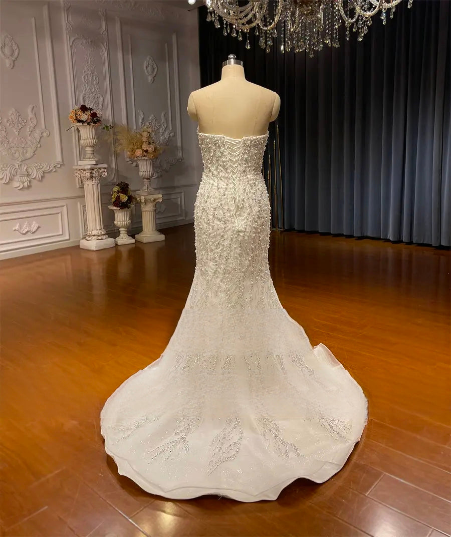 Rear view of the mermaid bridal gown on a mannequin, featuring a classic corset-style lace-up back and a graceful, flared train with delicate shimmer.