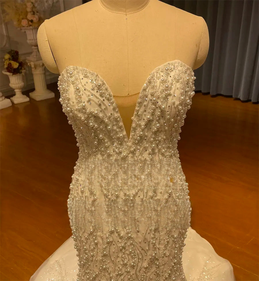 A detailed close-up of the strapless wedding dress bodice, focusing on the luxury pearl and crystal beadwork, sweetheart neckline, and sheer illusion plunge.