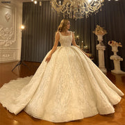Full-length front view of an elegant model wearing a thick strap ball gown wedding dress featuring a square neckline, heavy silver crystal beading, and a voluminous cathedral train in a bridal showroom.