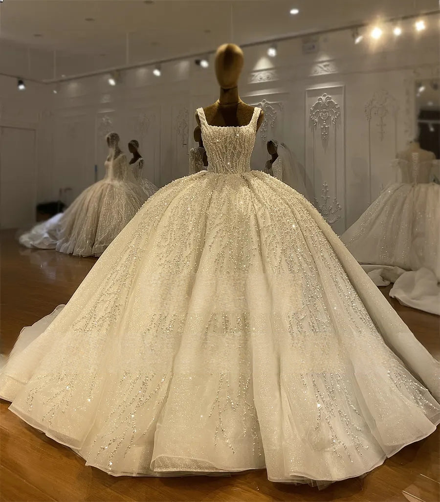 Showroom display of a luxury square neck bridal ball gown on a mannequin, highlighting the intricate branch-patterned crystal embroidery and massive sparkling skirt.