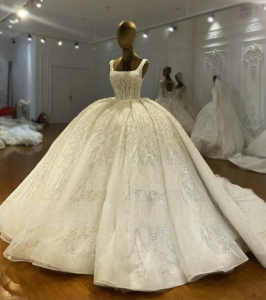 Side profile view of a heavily beaded ball gown wedding dress on a mannequin, showcasing the structured waistline and the elegant drape of the sparkling, embellished tulle skirt.