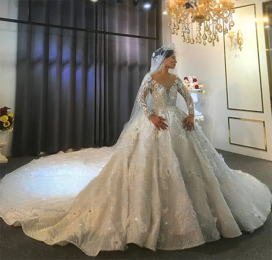 Full-length angled view of a bride modeling the stunning off-white bridal gown in a showroom, displaying the massive heavily beaded train and luxurious ball gown silhouette.