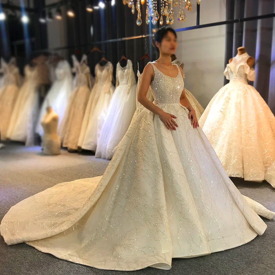 Elegant model wearing a stunning sleeveless luxury ball gown wedding dress with a heavily beaded bodice and a grand cathedral train, posing in a bridal showroom.