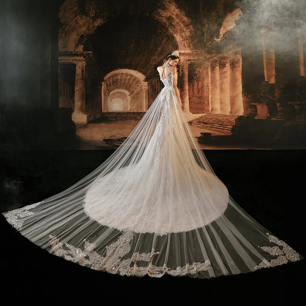 Rear perspective of a bride in a sparkling mermaid wedding dress, showcasing the dramatic spread of the sheer tulle cape overlay blending into a majestic, embellished cathedral-length train.