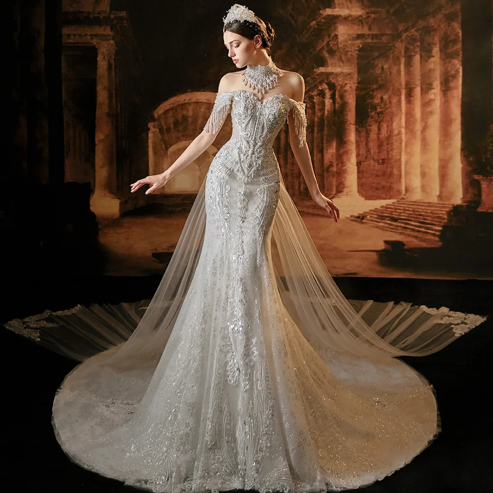 Full front portrait of a bride posing in a stylish luxury mermaid wedding dress with an intricate beaded high-neck choker, crystal tassel sleeves, and an expansive sheer overlay train.