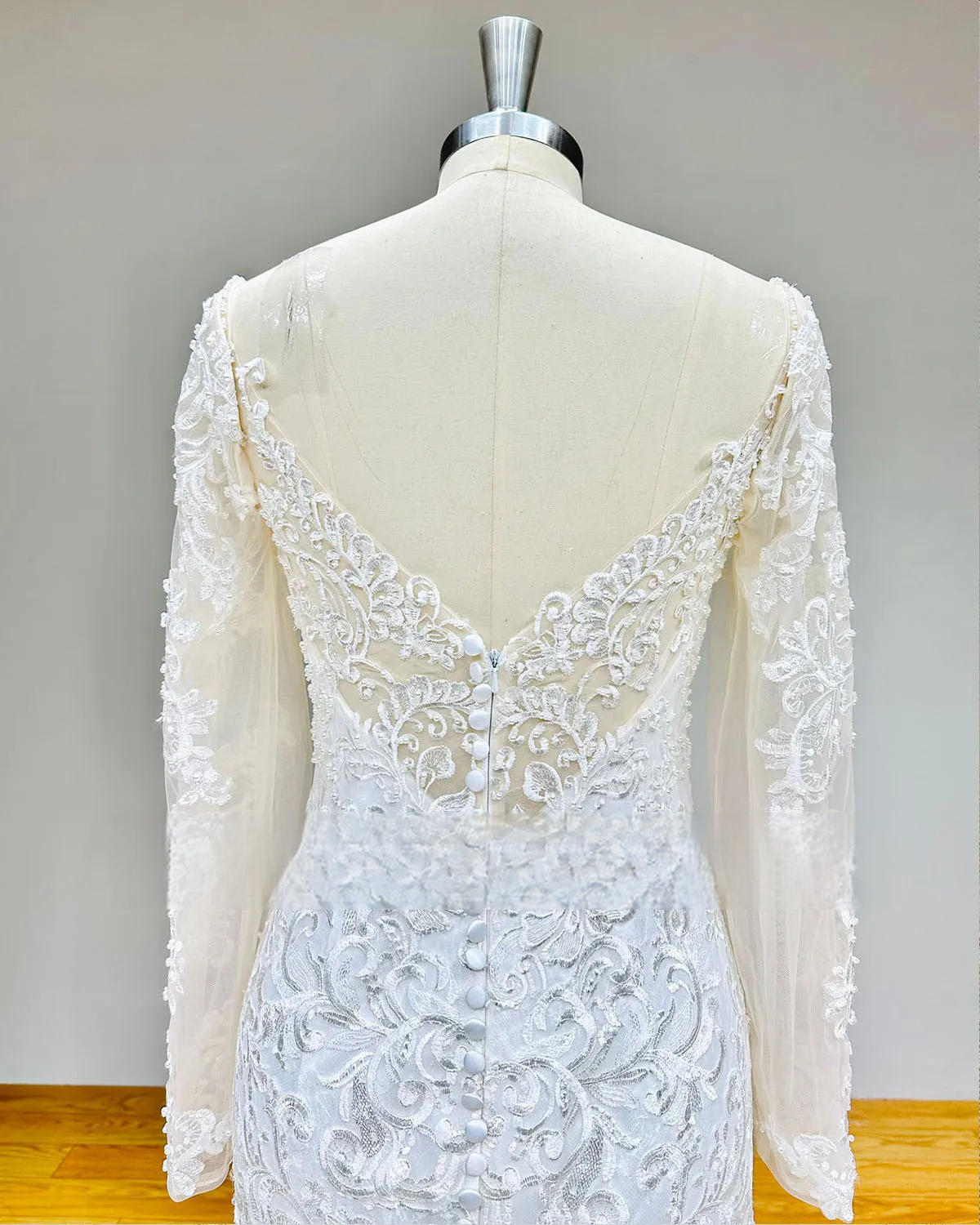 Rear perspective of the backless mermaid wedding gown highlighting the deep V-back design, bridal button row, and sheer lace sleeves.