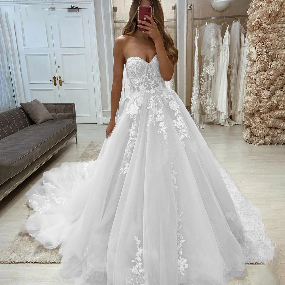 A bride wearing a gorgeous sweetheart sleeveless wedding dress with intricate floral lace appliqués and a flowing princess-style tulle skirt.