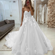 A bride wearing a gorgeous sweetheart sleeveless wedding dress with intricate floral lace appliqués and a flowing princess-style tulle skirt.