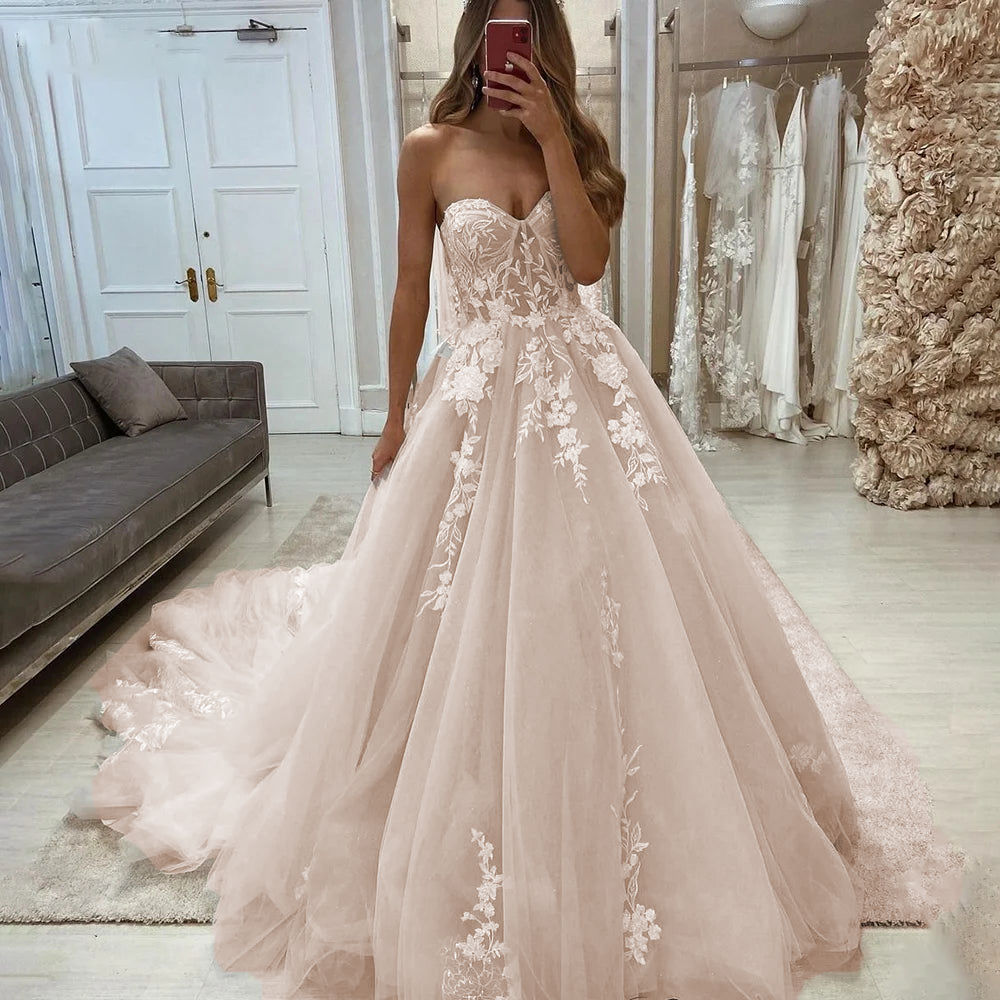 A bride modeling a romantic sweetheart sleeveless wedding dress with a full tulle skirt and detailed floral lace appliqués, perfect for a boho or princess-themed wedding.