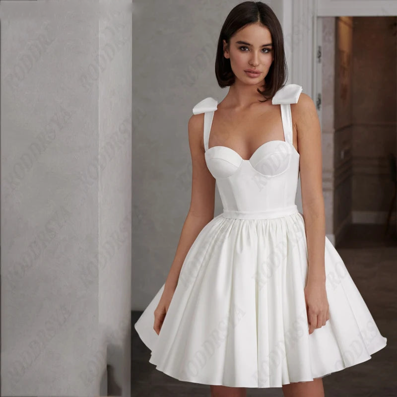 Close-up of a short white bridal gown featuring a sweetheart neckline, delicate straps with bow accents, and a flared A-line skirt.
