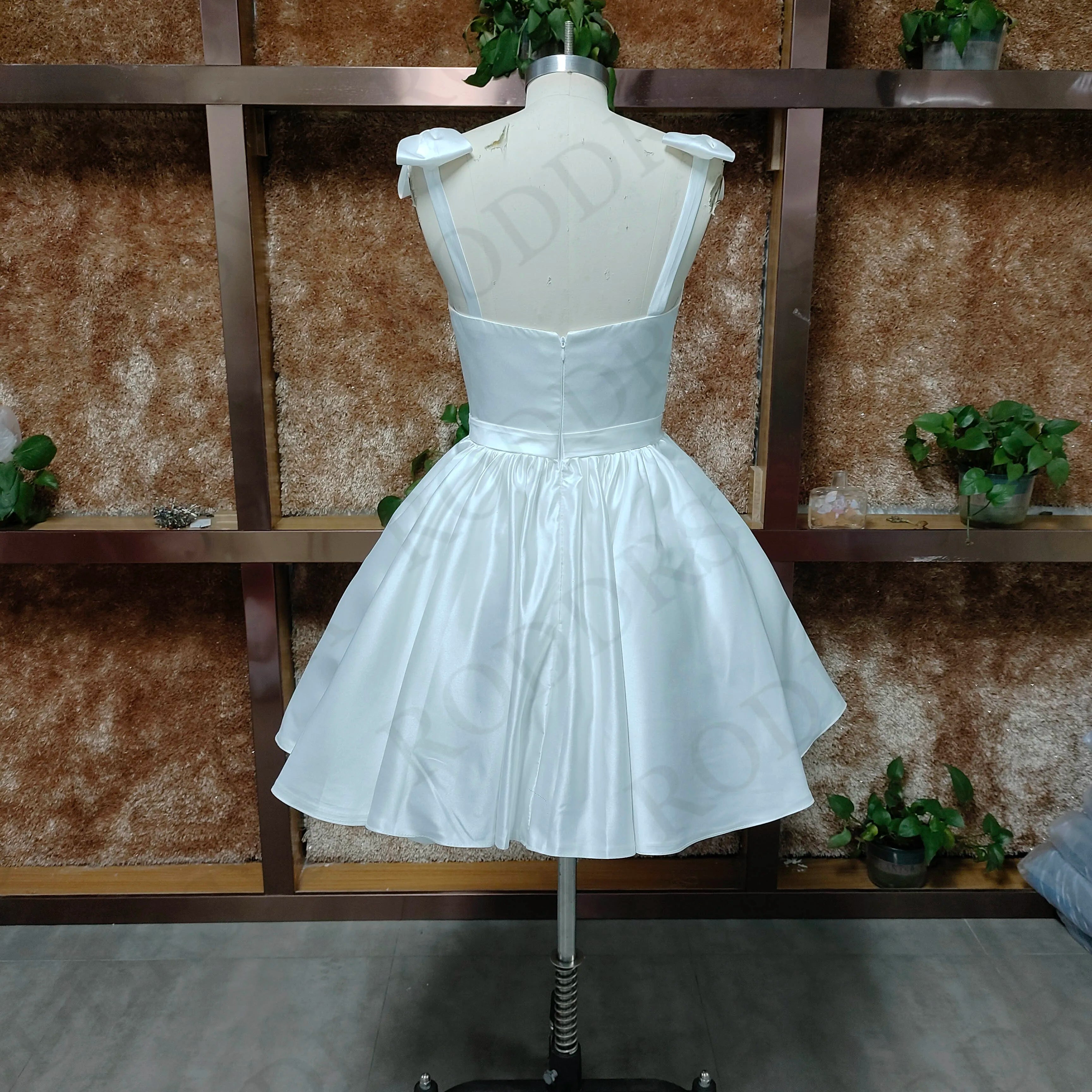 A rear view of a mannequin wearing a backless white mini wedding dress with a structured bodice and pleated A-line skirt.