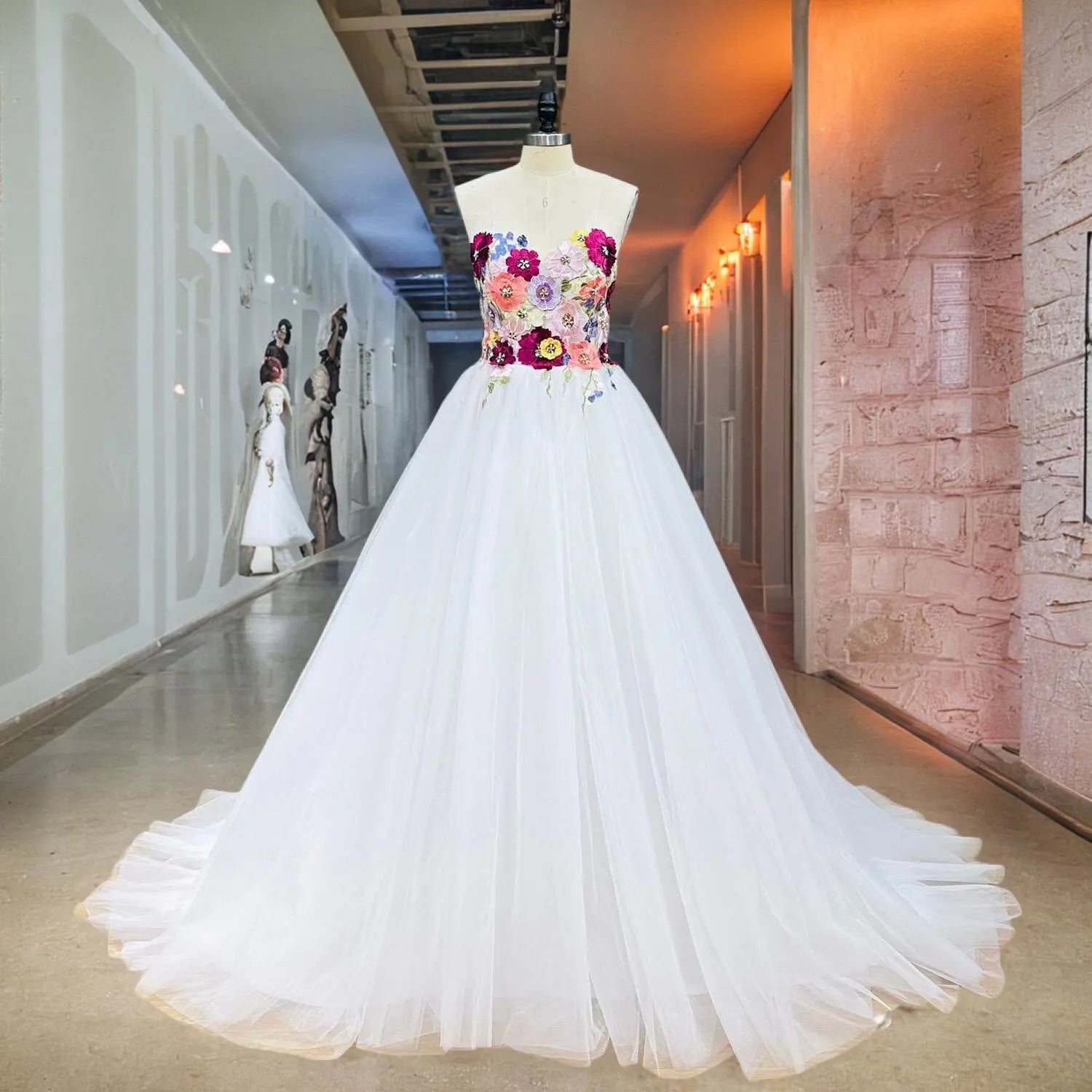 Showroom display of a strapless white tulle wedding dress on a mannequin, highlighting the intricate colorful floral appliques on the sweetheart bodice.