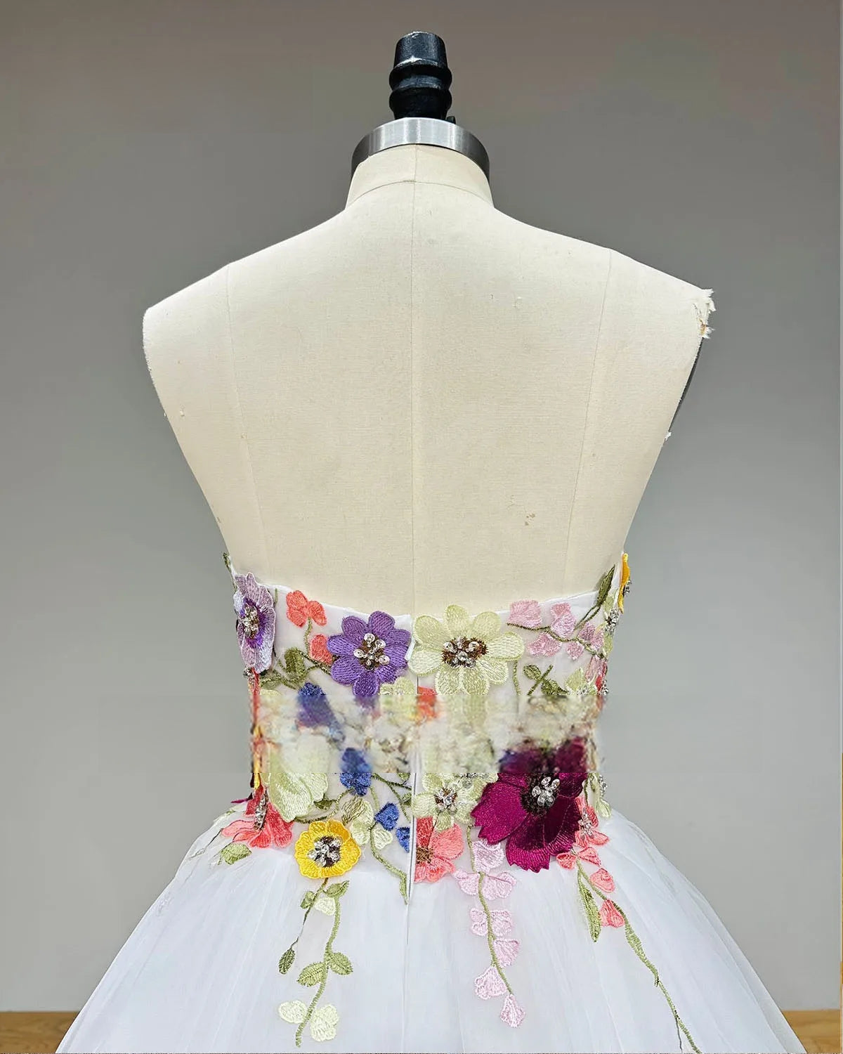 Close-up of the back of the wedding dress bodice on a mannequin, showcasing the continuing colorful floral embroidery and subtle zipper back closure.