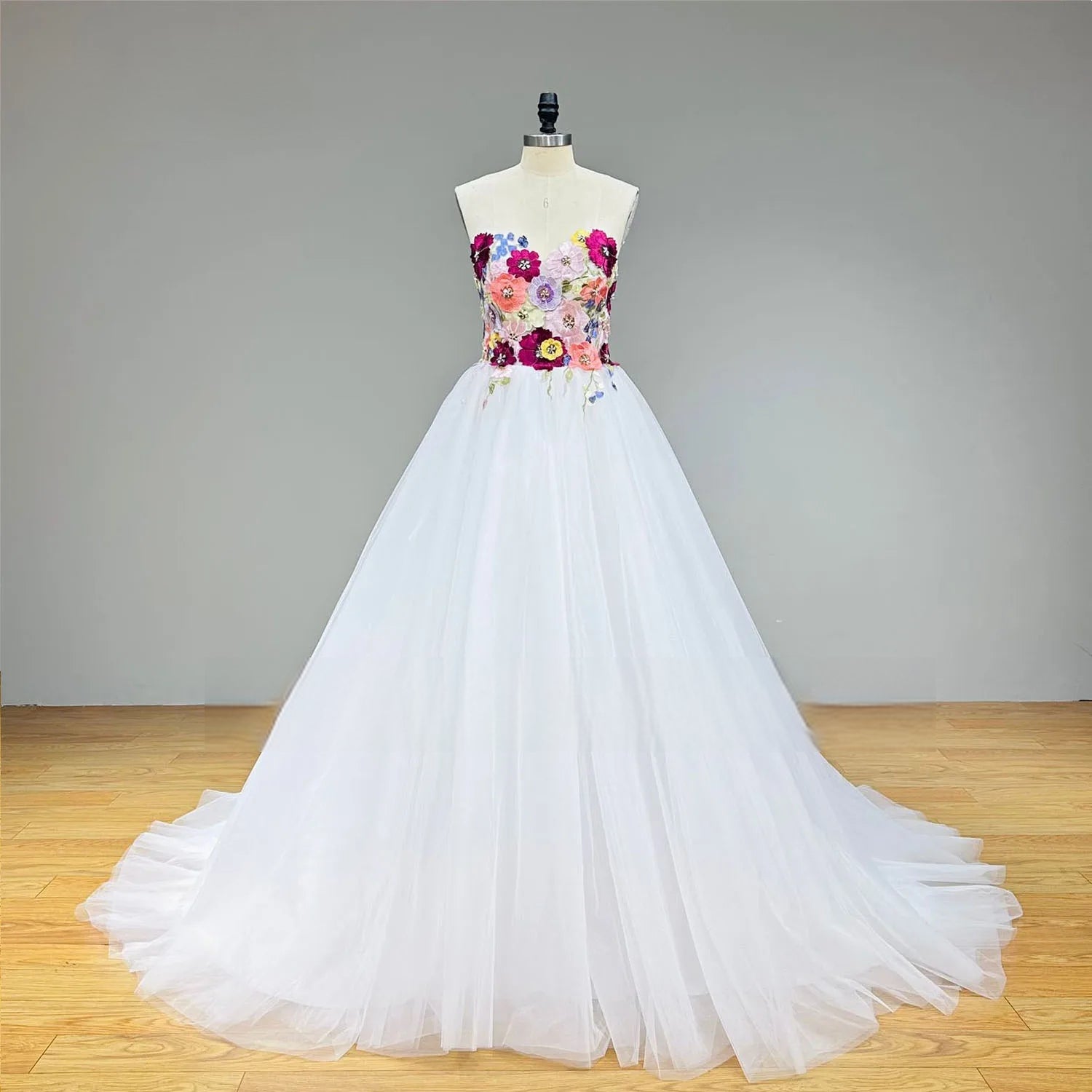 Studio front view of a white ball gown wedding dress on a mannequin, emphasizing the striking contrast of the vibrant floral beaded bodice against the pure white tulle skirt.