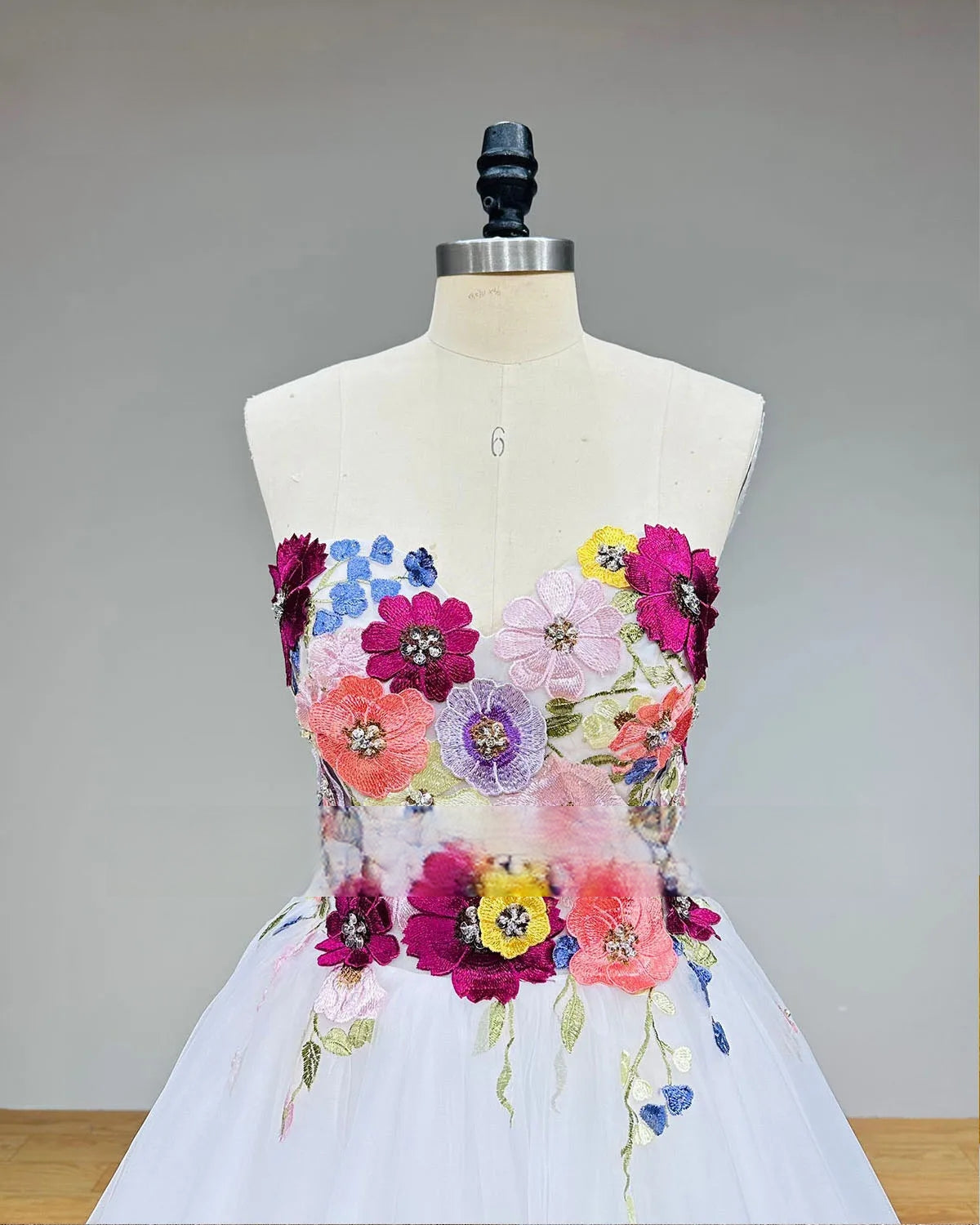 Detailed close-up of the front bodice on a mannequin, showcasing the exquisite craftsmanship of the colorful floral appliques, beads, and sequins on the sweetheart