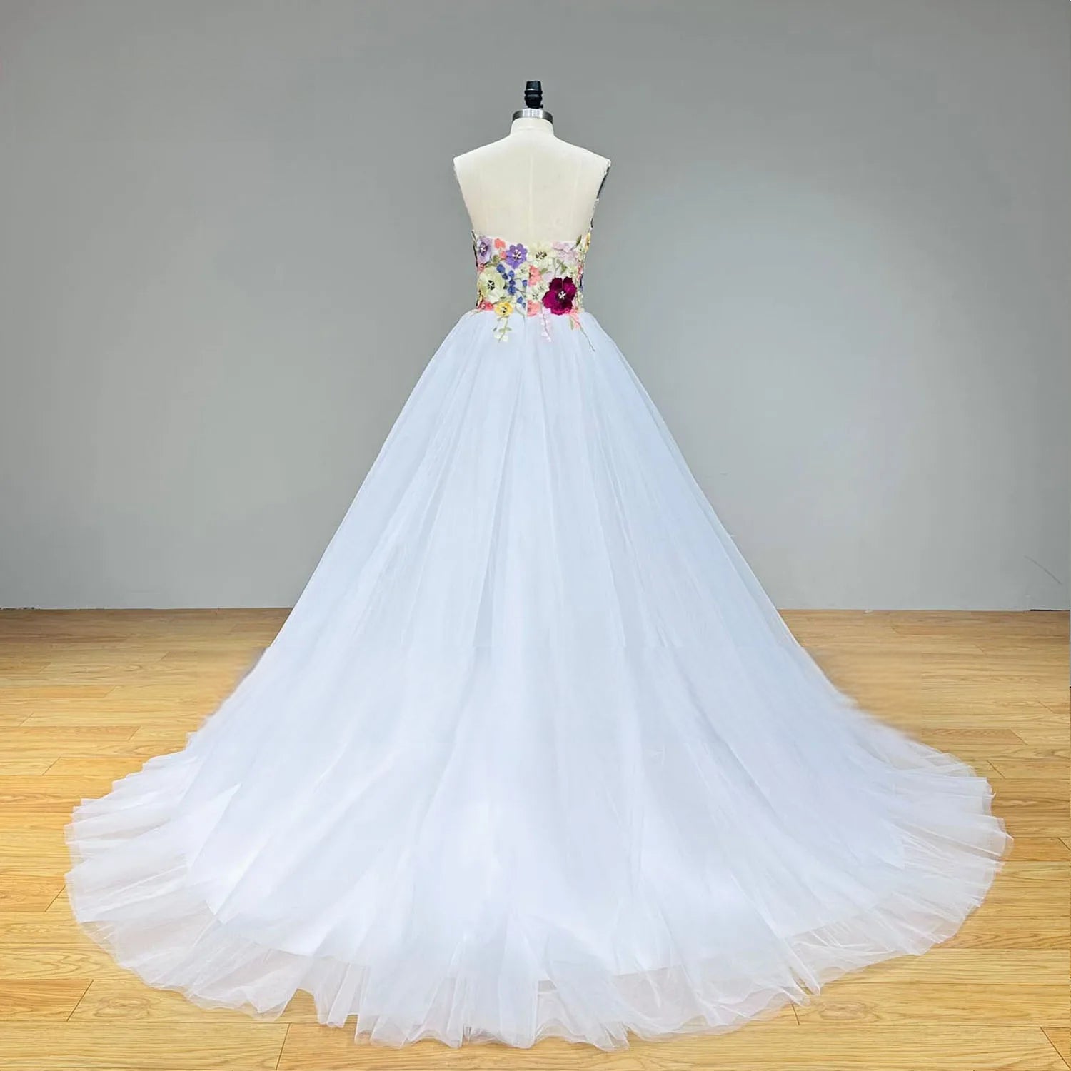 Full-length rear view of the white tulle wedding dress on a mannequin, highlighting the seamless transition from the colorful floral bodice to the sweeping plain tulle train.