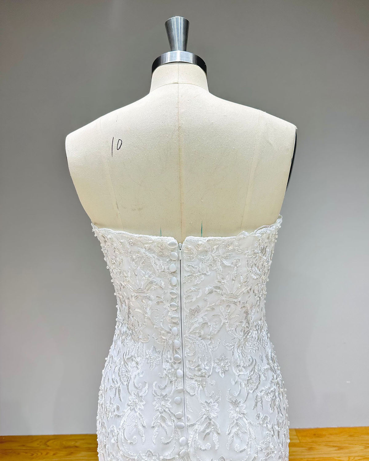 Close-up of the back of a strapless bridal dress showcasing the zipper closure hidden beneath elegant fabric-covered bridal buttons and lace embroidery.