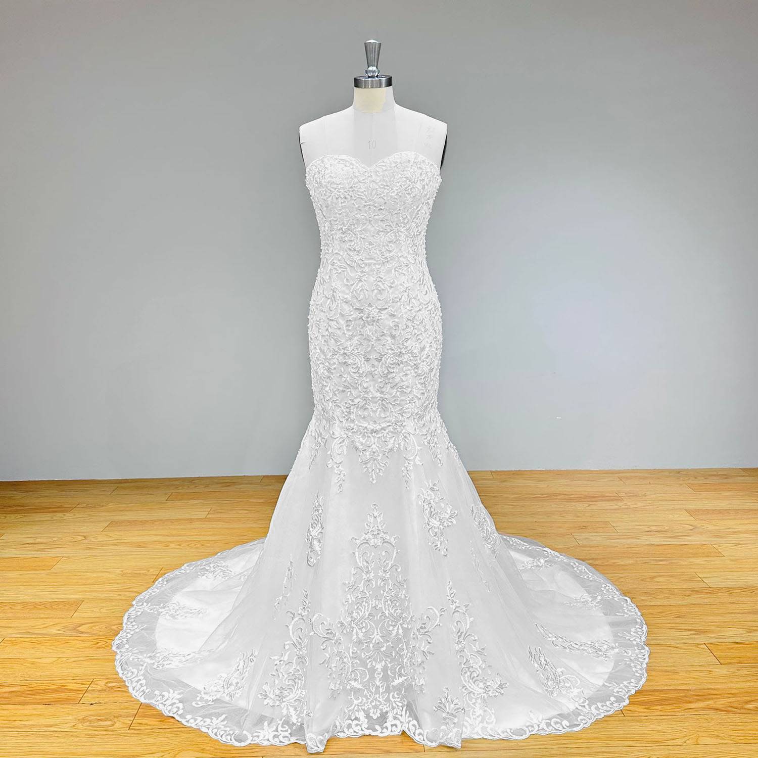 Front view of a strapless sweetheart neck lace mermaid wedding gown with a dramatic flared tulle and lace scalloped skirt on a dress form.