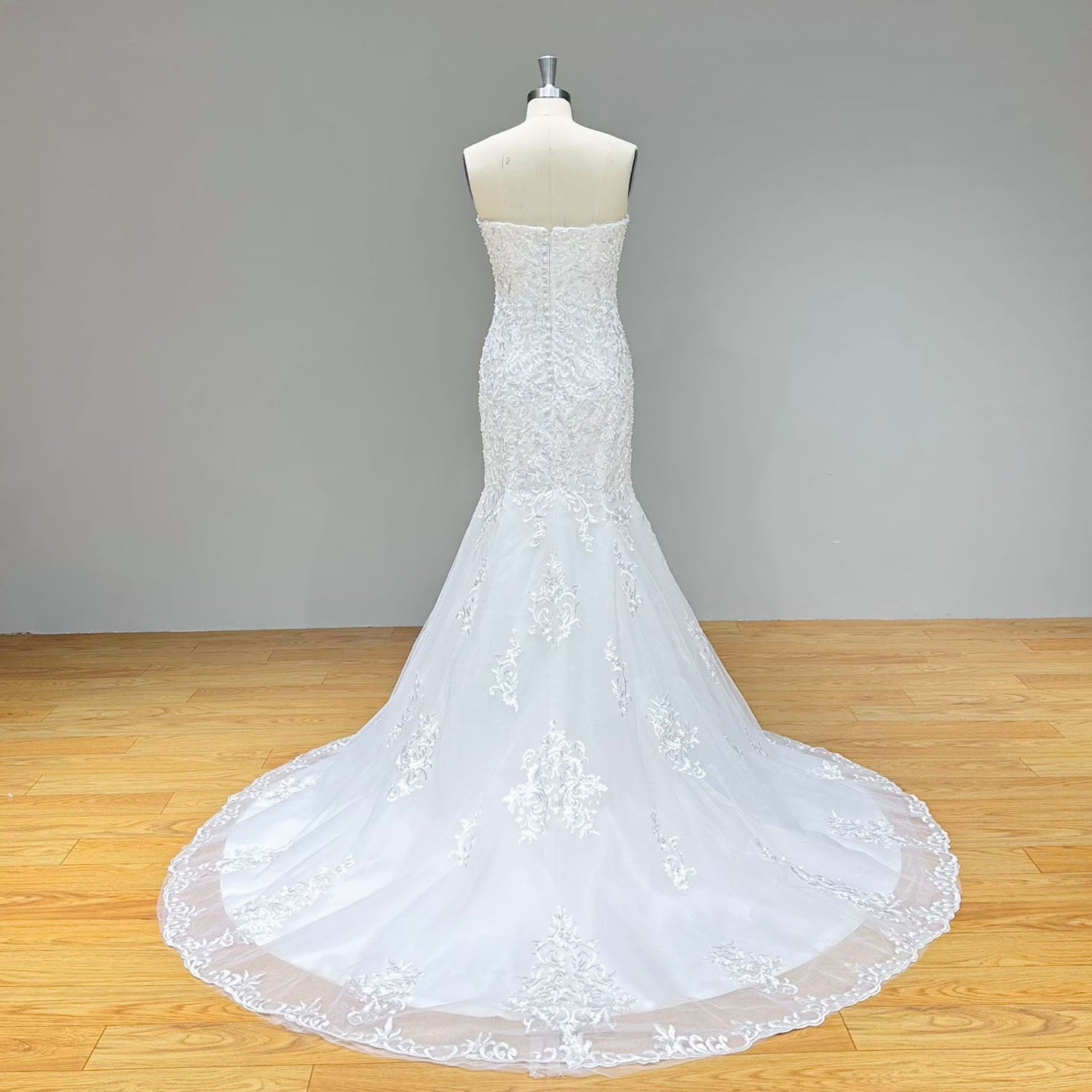 Back view of a strapless mermaid wedding dress showing a structured bodice, covered button details over a zipper back, and a lace-trimmed train.