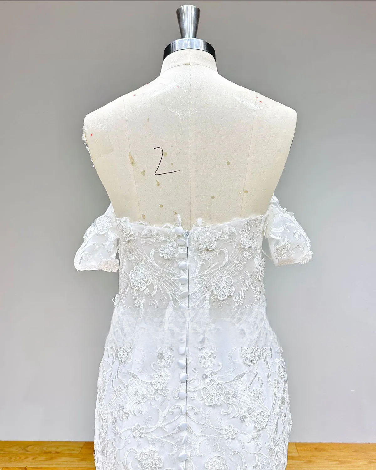 Detailed rear view of a mermaid wedding dress bodice on a mannequin, featuring a sheer lace illusion back with an elegant row of bridal buttons.