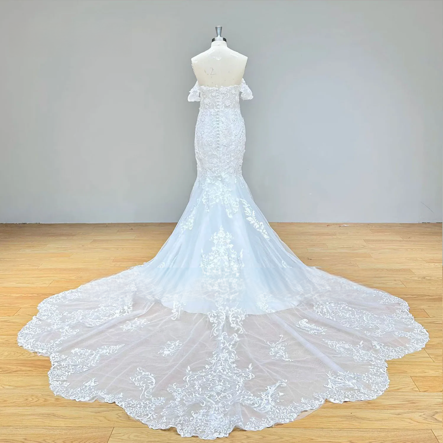 Detailed rear view of a mermaid wedding dress bodice on a mannequin, featuring a sheer lace illusion back with an elegant row of bridal buttons.