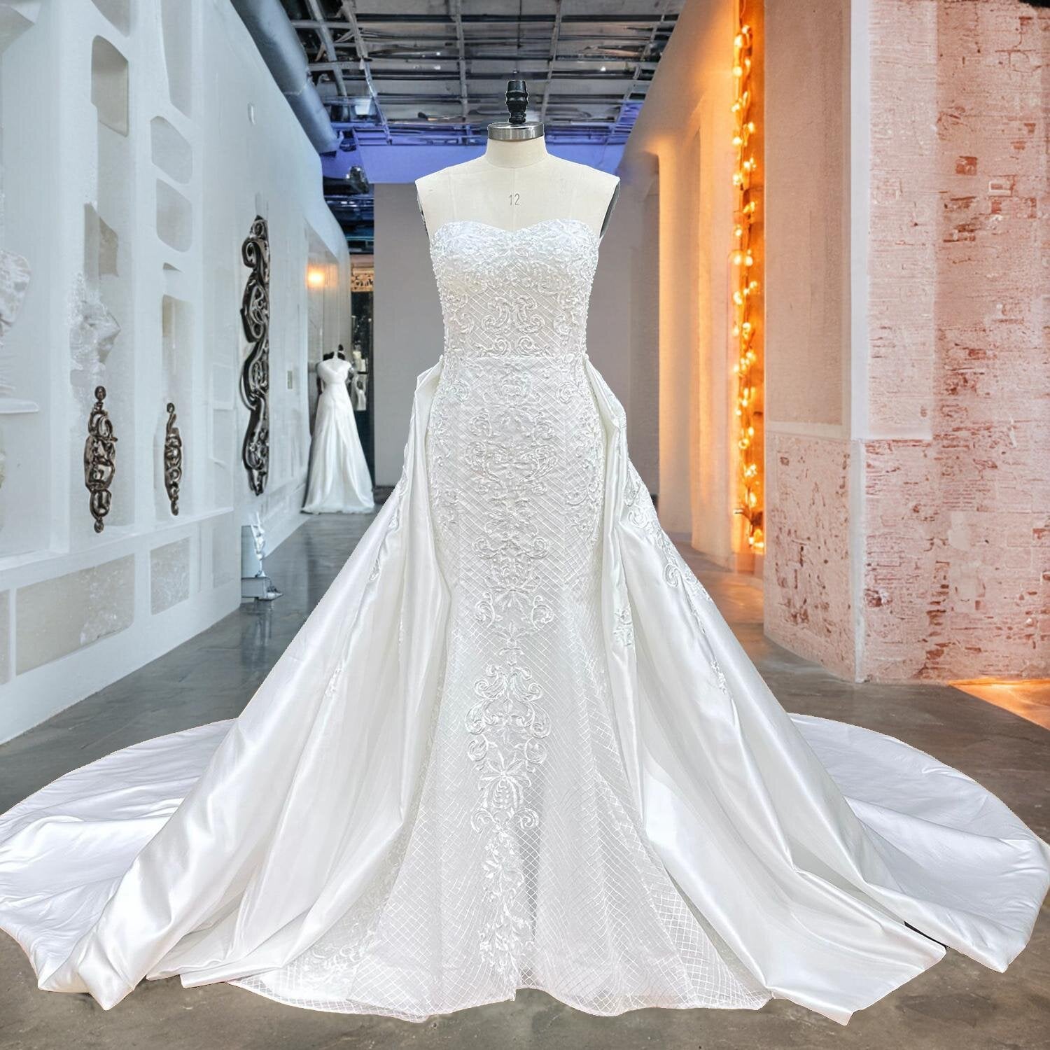 Full front view of a sweetheart neck mermaid wedding dress on a mannequin in a studio hallway, perfectly displaying the added dramatic volume of the sheer lace detachable train.