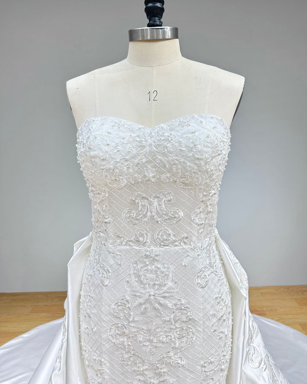 Close-up front bodice detail of a sweetheart neck mermaid wedding dress on a mannequin, emphasizing the off-the-shoulder sheer lace sleeves, plunge neckline, and intricate floral beadwork.