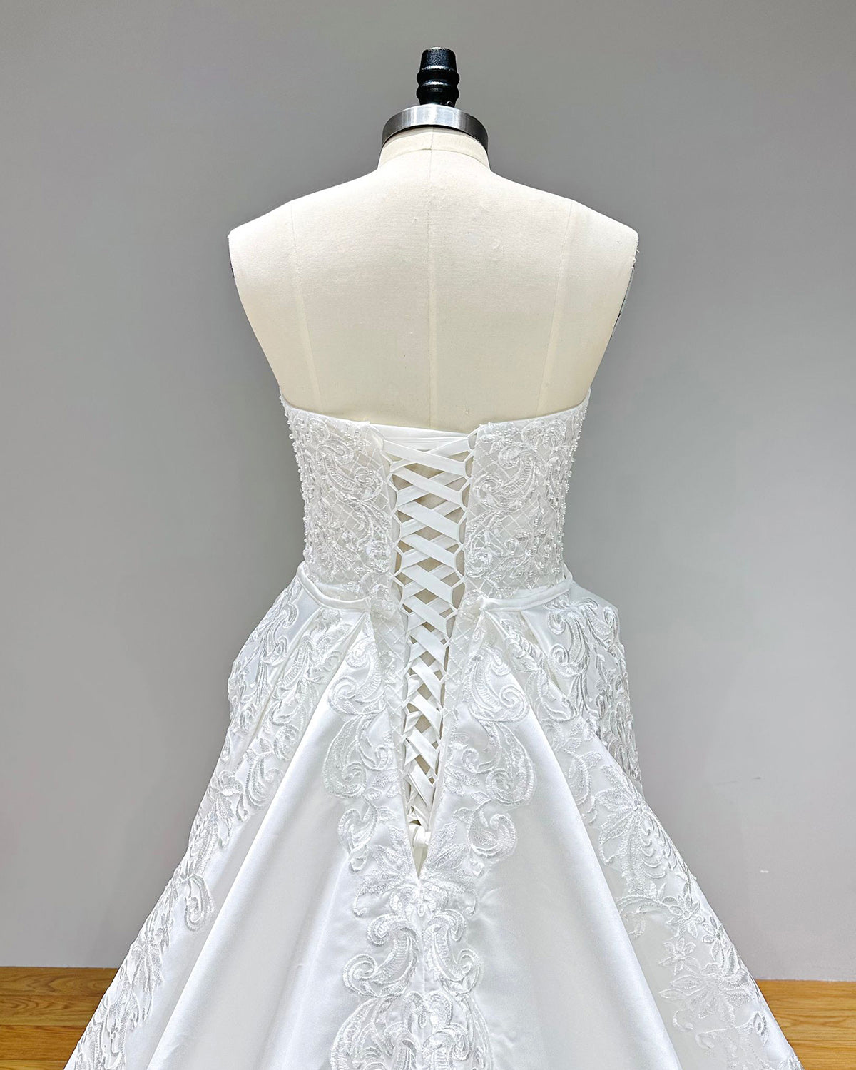 Dramatic full back view of an off-the-shoulder sweetheart neck mermaid wedding dress on a mannequin, highlighting the classic lace-up corset back and wide, sweeping detachable train.