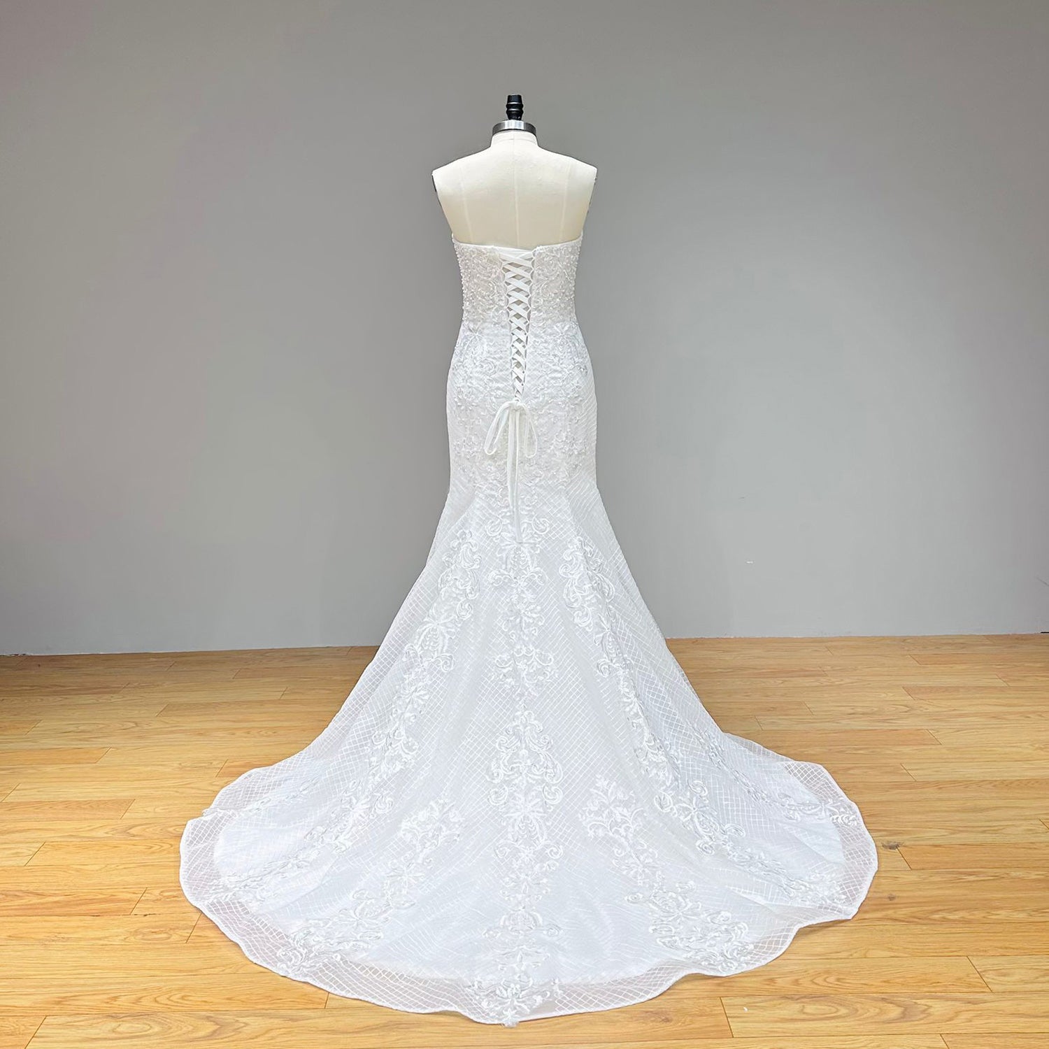 Angled side-back view of a sweetheart neck mermaid wedding dress on a mannequin, showing the layered volume of the attached detachable train, lace-up back, and sparkling floral lace appliques.