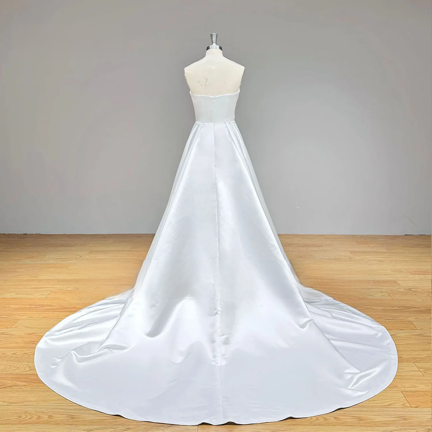 Rear view of a minimalist satin A-line wedding dress on a mannequin, highlighting the clean zipper back closure and a sweeping chapel-length train.