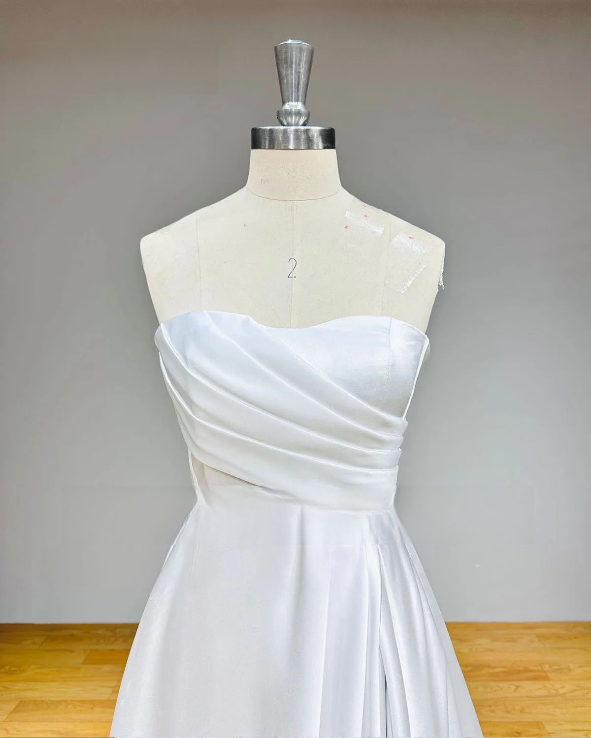 Close-up detail of a bridal bodice on a mannequin, showcasing the elegant sweetheart neckline and intricate hand-pleated satin fabric.