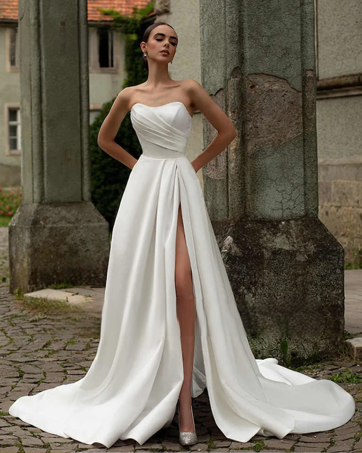 A bride posing outdoors in a strapless sweetheart neck satin A-line wedding dress, highlighting the daring high leg slit and elegant flowing fabric.