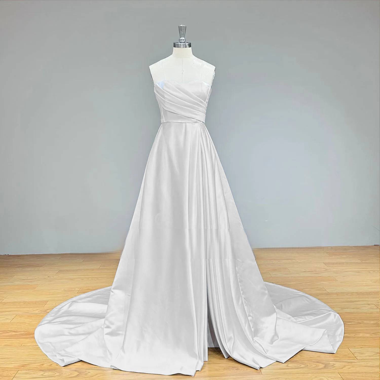 Studio display of a white satin A-line bridal gown with a sweetheart neckline and a long, pleated skirt featuring a modern side slit.