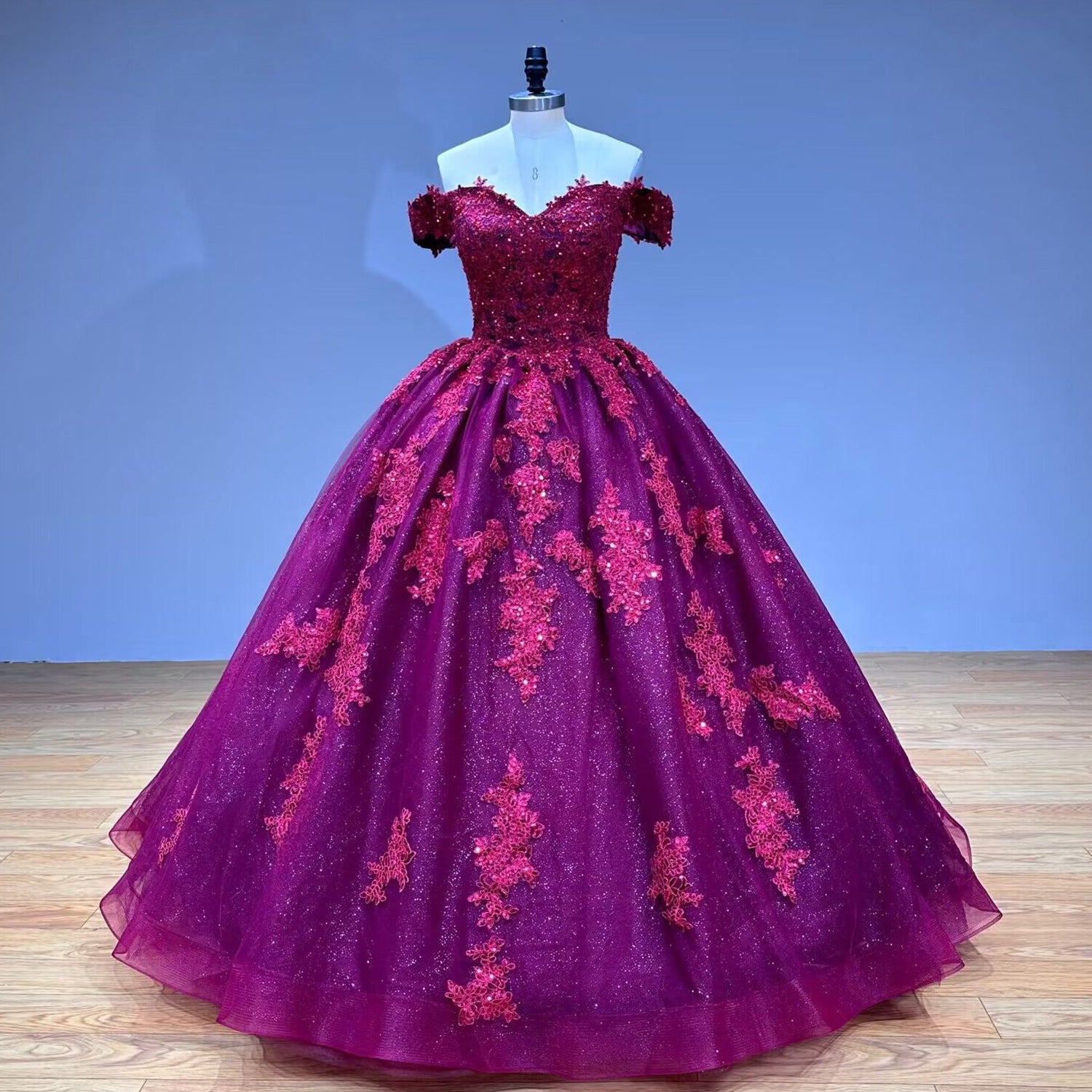 Studio product photography showcasing the full front view of a sweetheart neck burgundy ball gown with a glittering tulle skirt and embroidered lace on a mannequin.
