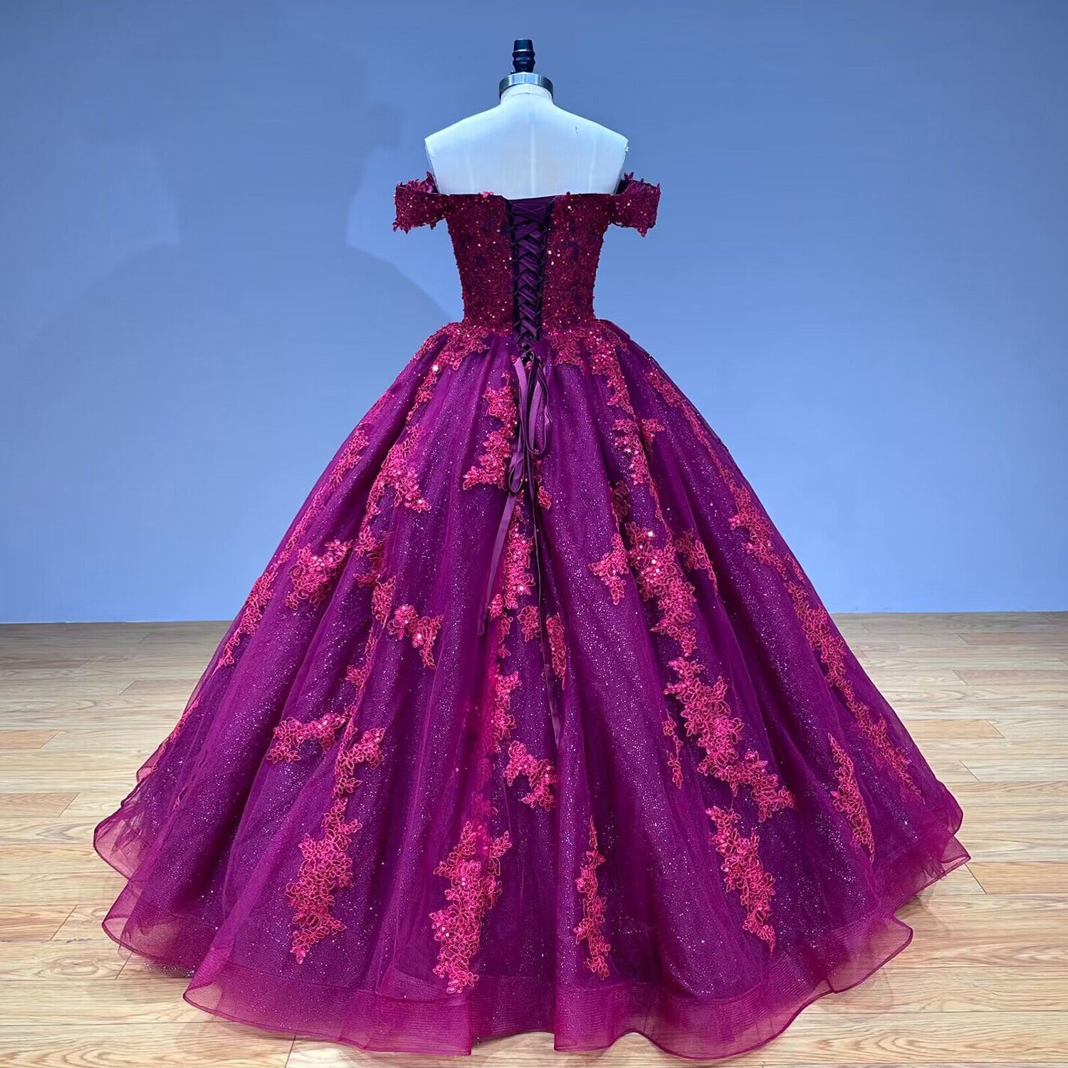 Full back view of the burgundy lace-up formal dress on a mannequin, showcasing the satin corset back and scattered floral appliques down the voluminous skirt.
