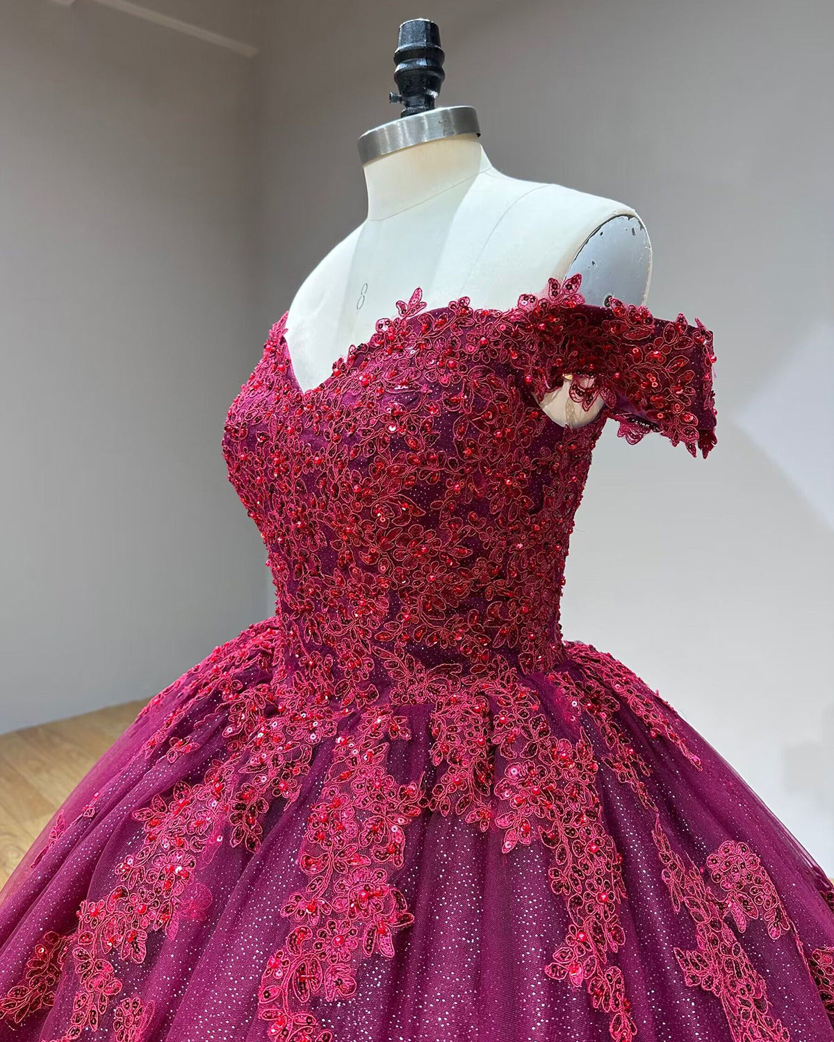 Three-quarter side profile detail of the off-the-shoulder burgundy dress bodice, showcasing the delicate short sleeves and heavy crystal beadwork on a studio mannequin.