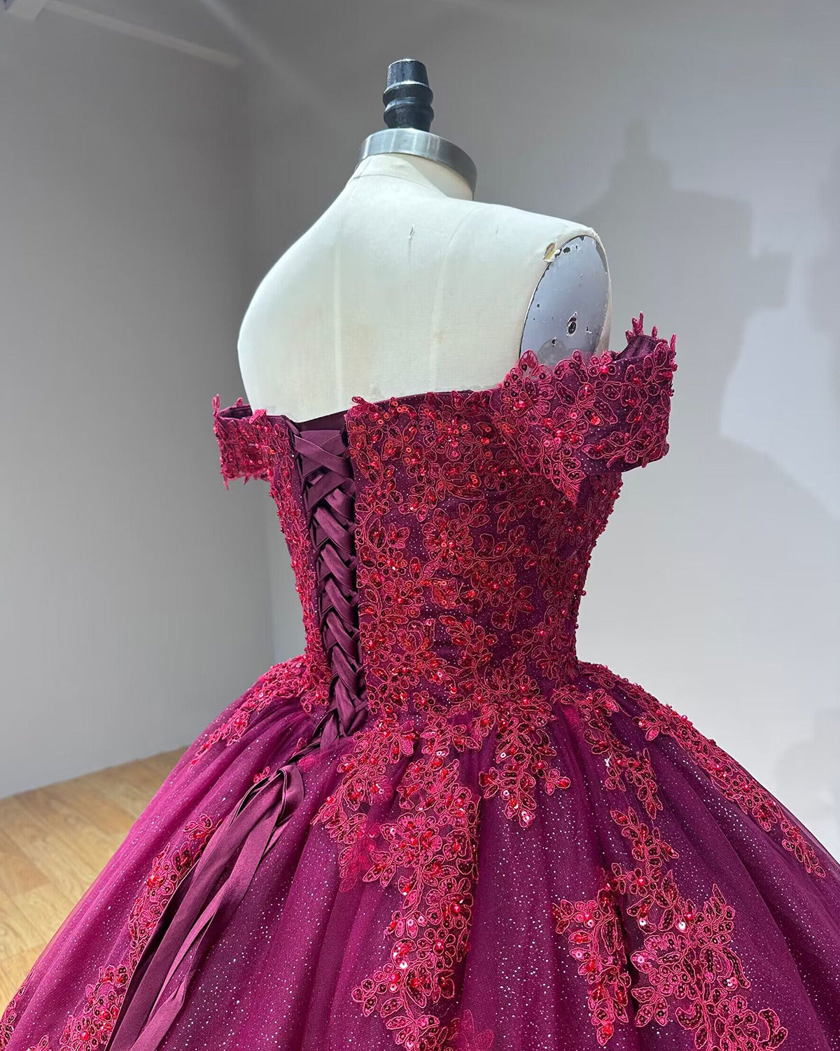 Angled close-up of the dress back showing the satin ribbon lace-up corset closure and textured floral embroidery spreading over the glittering bodice.
