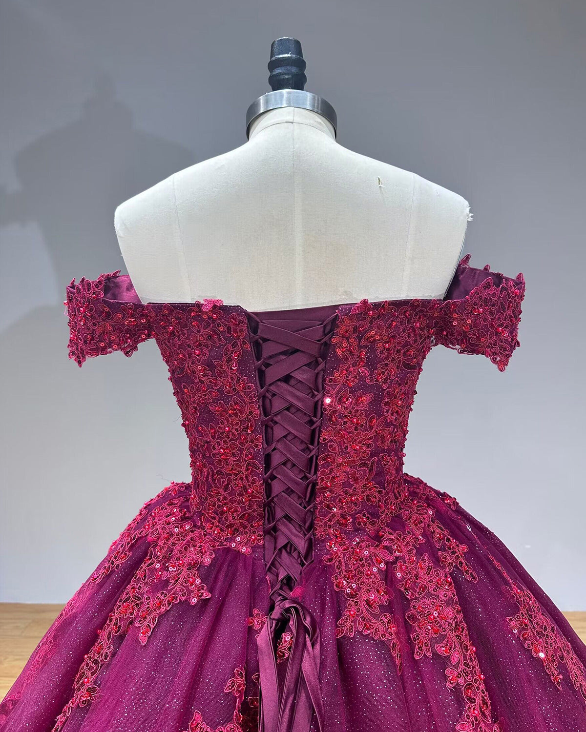 Detailed direct back view of the burgundy evening gown focusing on the symmetrical satin corset lacing system and heavily beaded floral lace detailing.