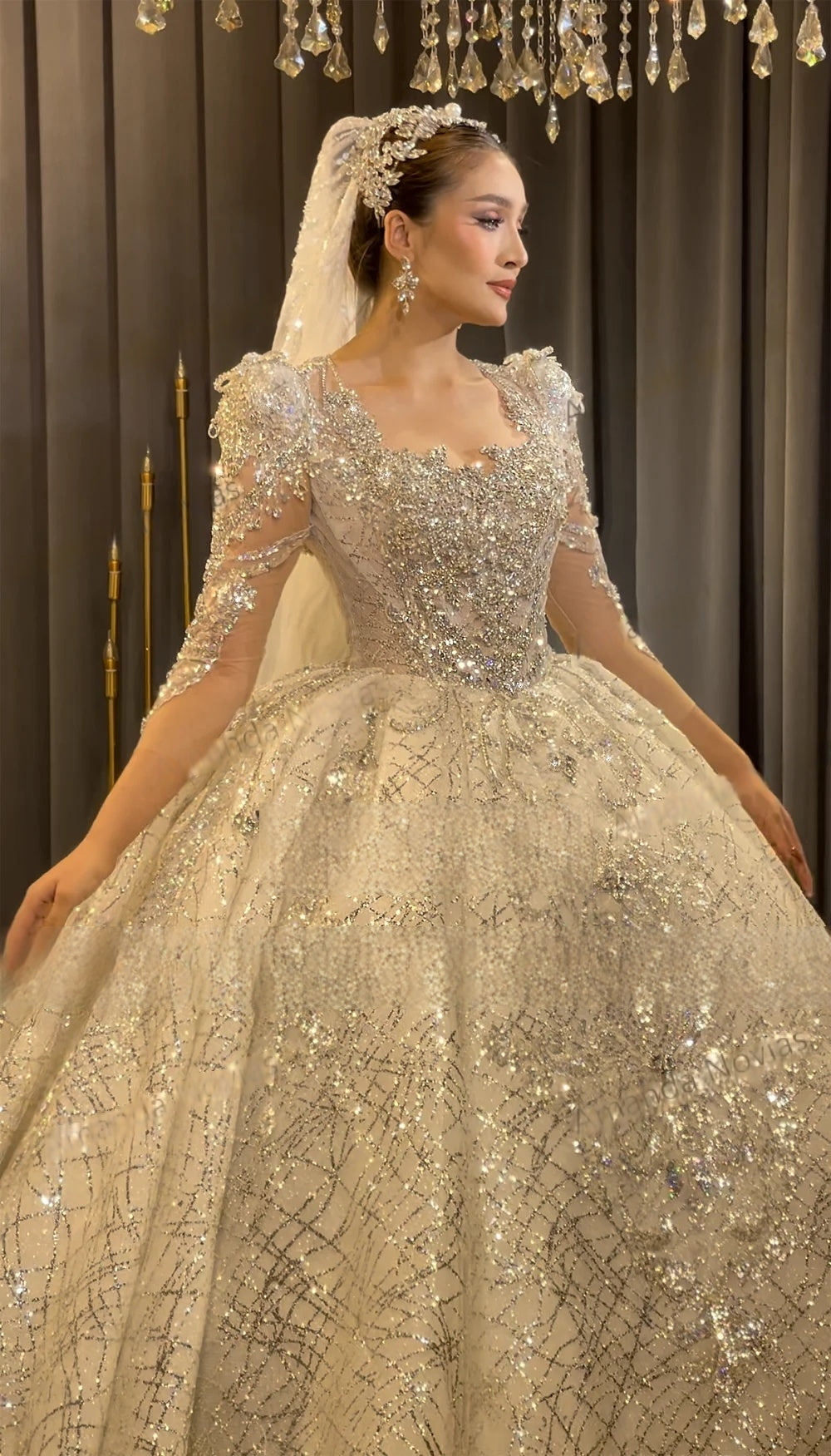 Side profile of a long-sleeved beaded bridal gown featuring puffed shoulders, intricate crystal embellishments, and a matching royal bridal crown and veil.