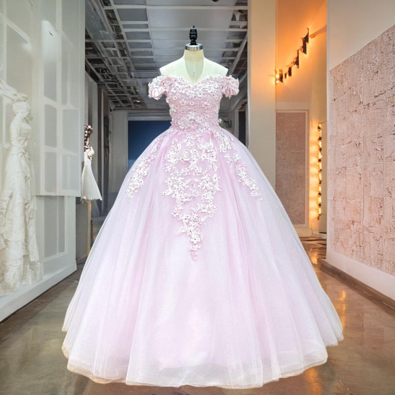 Full front view of a stunning sweetheart pink dress on a mannequin in a studio hallway, highlighting the classic ball gown silhouette decorated with delicate 3D flowers and sparkling crystals.