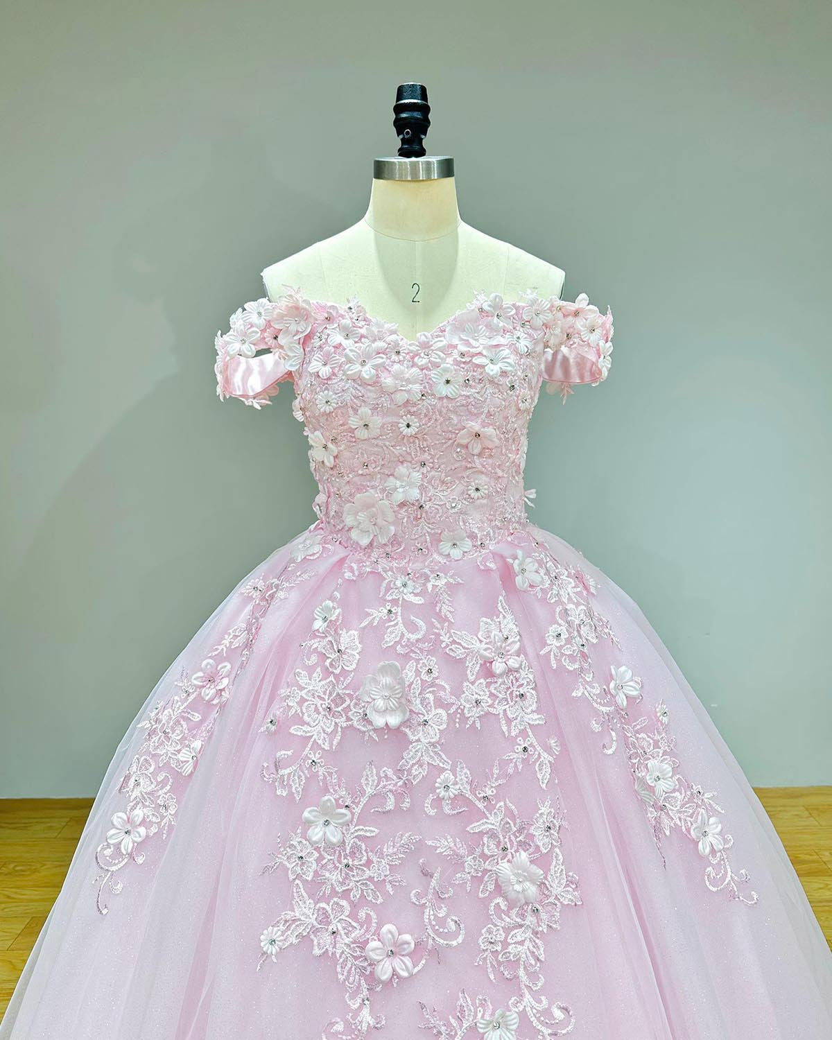 Close-up front bodice detail of a sweetheart pink dress on a mannequin, emphasizing the exquisite embroidery featuring 3D flowers, pearls, and shimmering crystals across the sweetheart neckline.