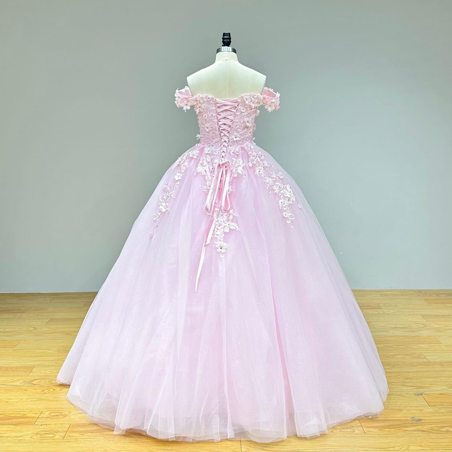 Full back view of a sweetheart pink dress on a mannequin, displaying the elegant lace-up back, off-the-shoulder straps, and a sweeping tulle skirt scattered with floral appliques.
