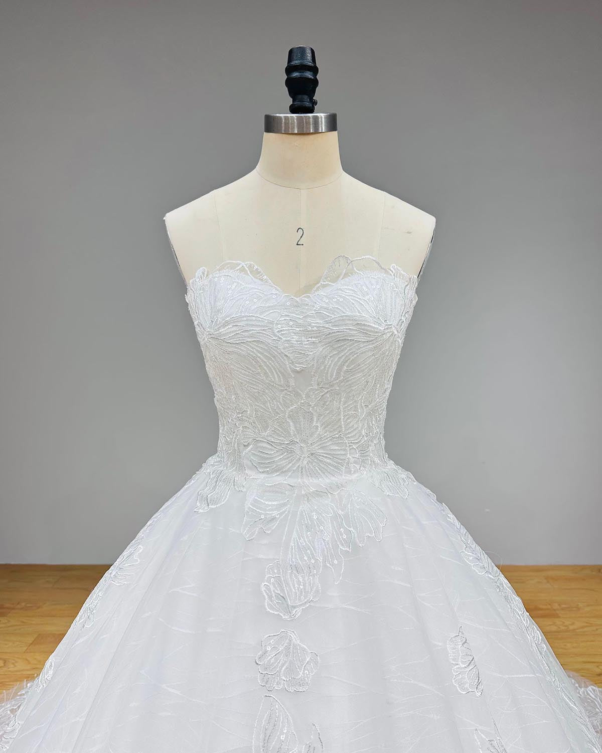 Dramatic full back view of a transparent sequined appliques ball gown wedding dress on a mannequin, perfectly displaying the traditional lace-up back and a wide, sweeping glitter train.