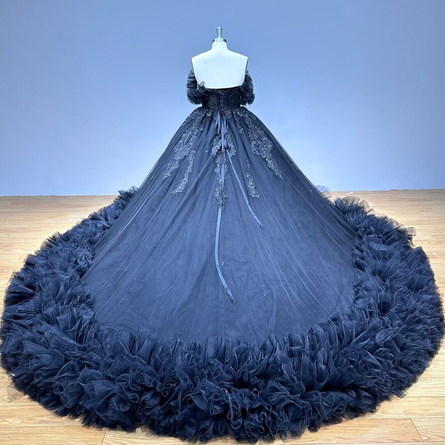 Full-length back studio view of a white tulle ball gown wedding dress on a mannequin, emphasizing a structured lace-up corset and a sweeping chapel-length train.