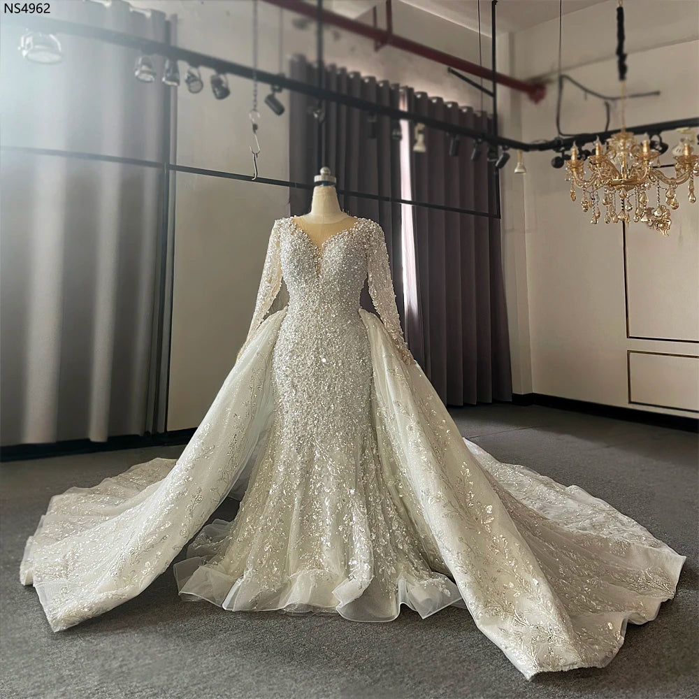 Full-length view of the heavily beaded mermaid wedding dress on a mannequin, highlighting the fitted silhouette and the grand spread of the detachable lace overskirt.