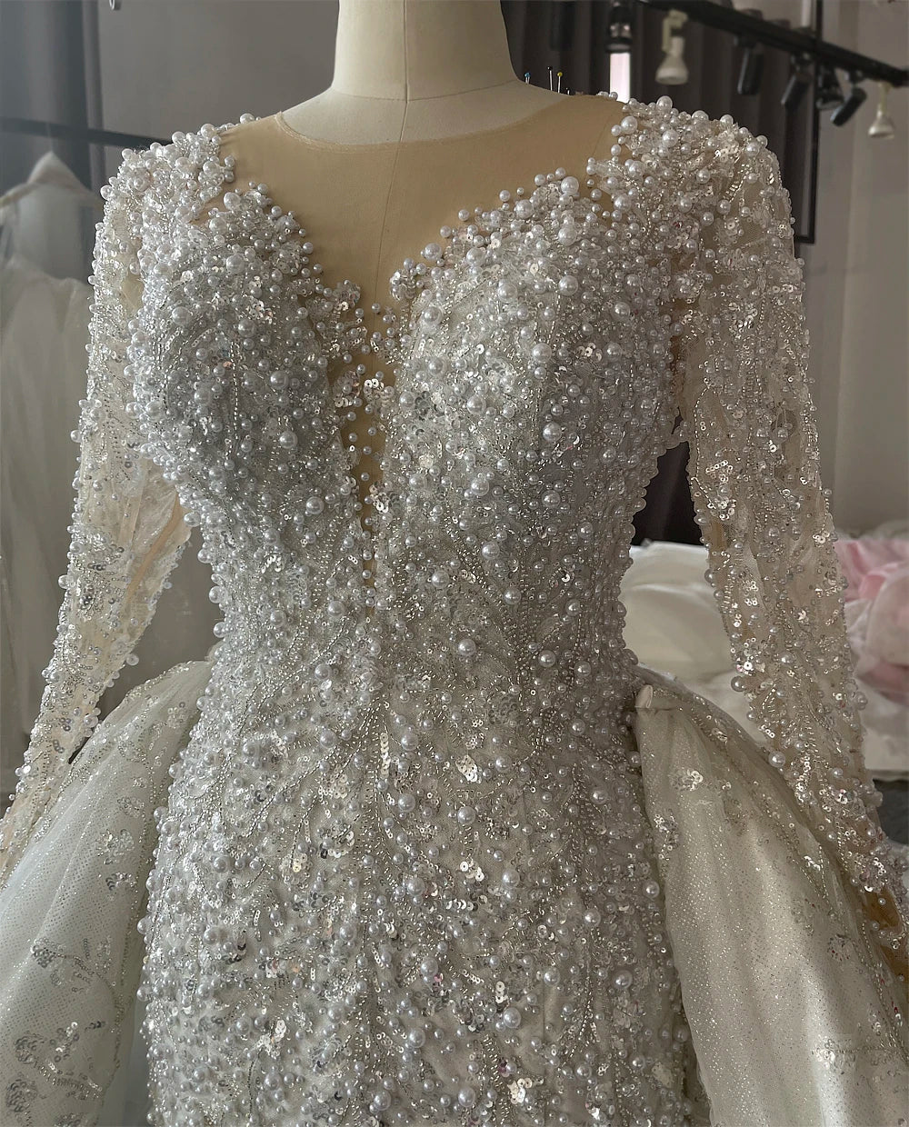 Close-up detail of the luxury bridal bodice, focusing on the exquisite heavy hand-beading, pearls, and shimmering sequins on a sheer high-neck illusion top.