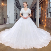 Full-length front view of an elegant bride wearing a V-neck short sleeve ball gown wedding dress, featuring a pearl-beaded diamond-pattern bodice and a voluminous skirt with scattered pearls.