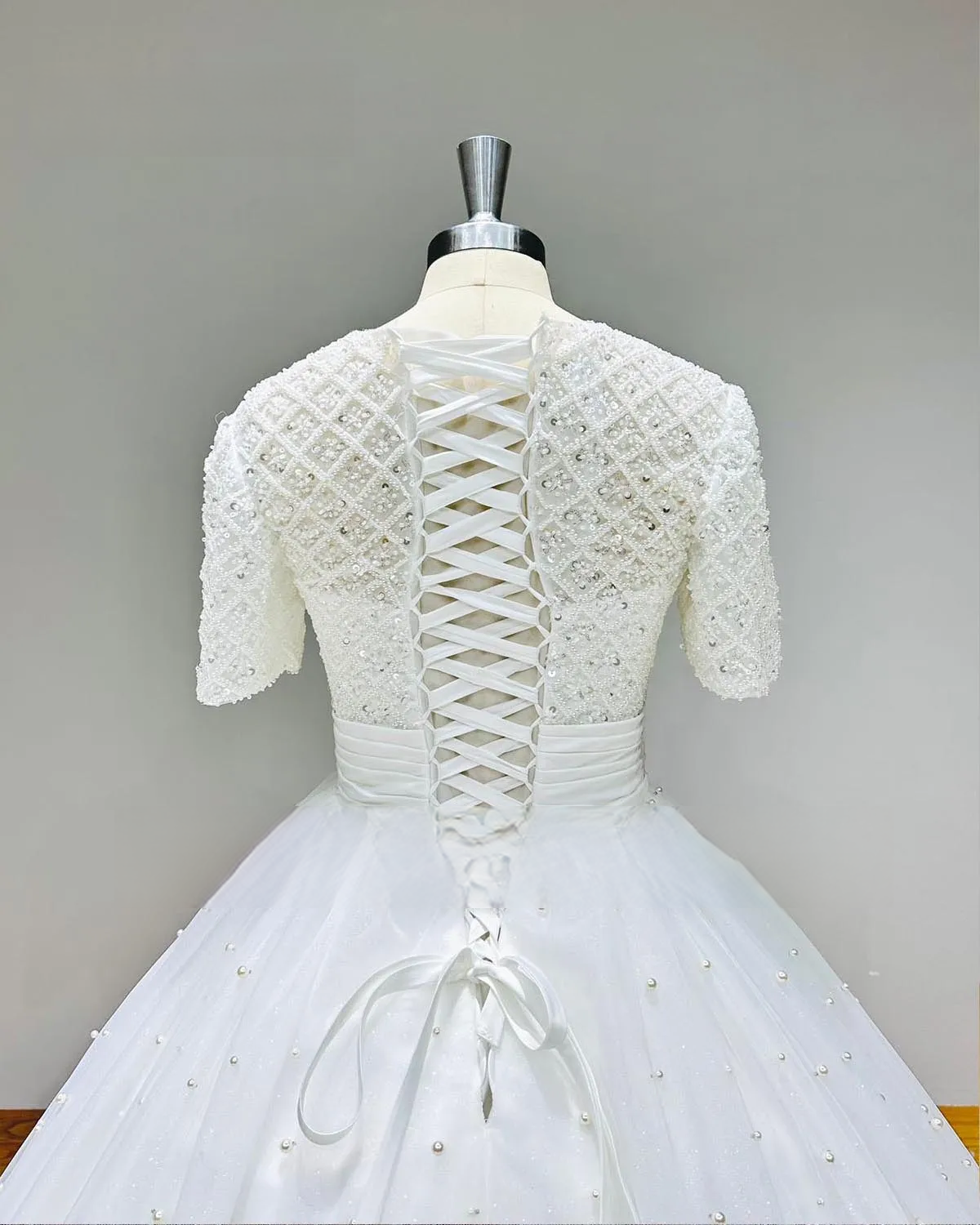 Detail shot of a bridal ball gown bodice featuring an intricate beaded diamond grid and a traditional white lace-up corset back.