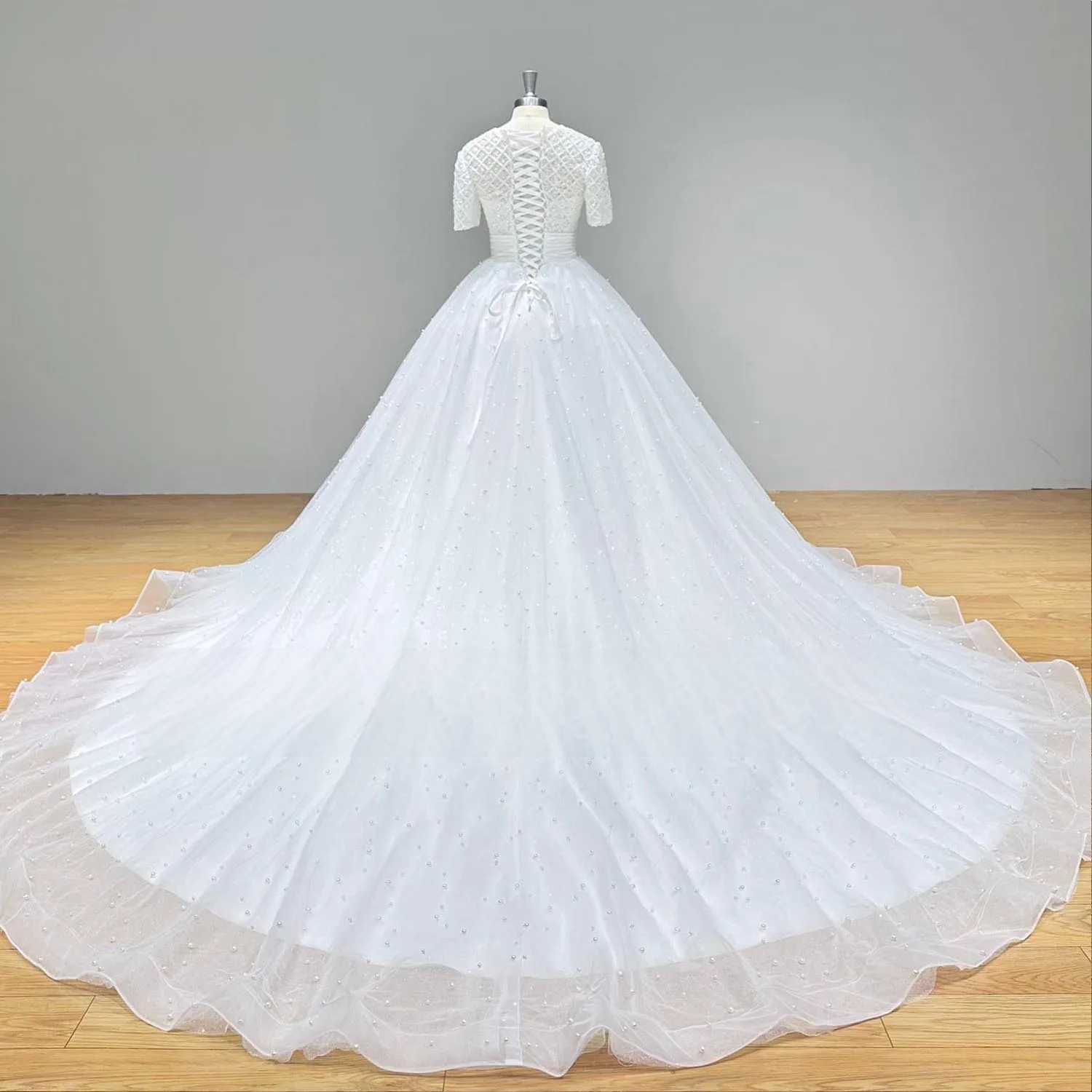 Rear perspective of a luxury white wedding dress highlighting a grand cathedral-length tulle train embellished with scattered pearls.