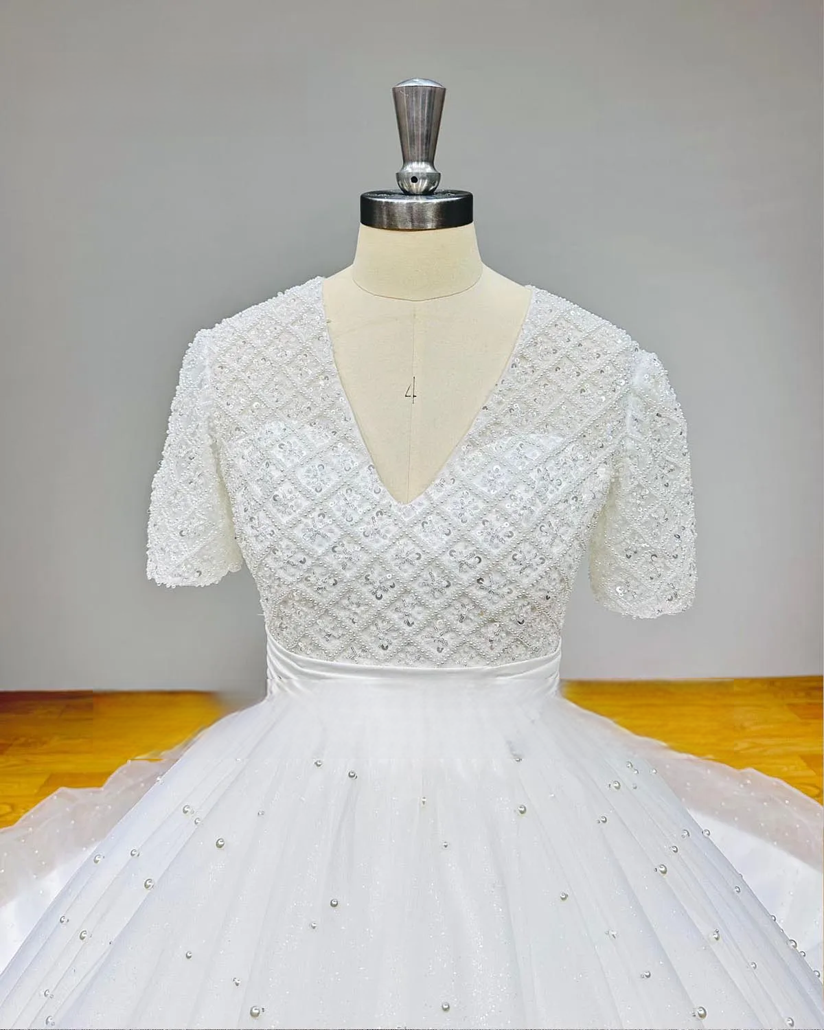 Close-up view of a V-neck bridal gown bodice showcasing handcrafted pearl beading and a sophisticated diamond pattern.